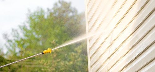 Someone pressure washing vinyl siding on their home